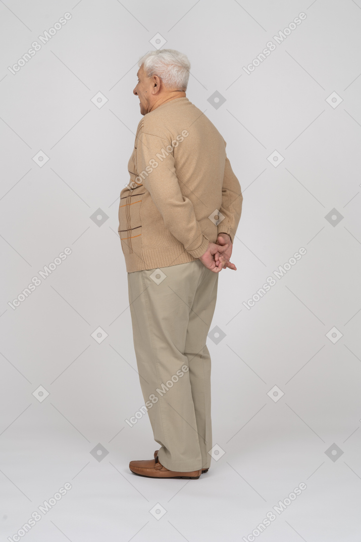 Side view of an old man in casual clothes standing with hands behind back