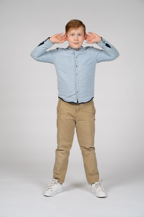 Vista frontal de um menino bonito de pé com as mãos na cabeça e olhando para a câmera