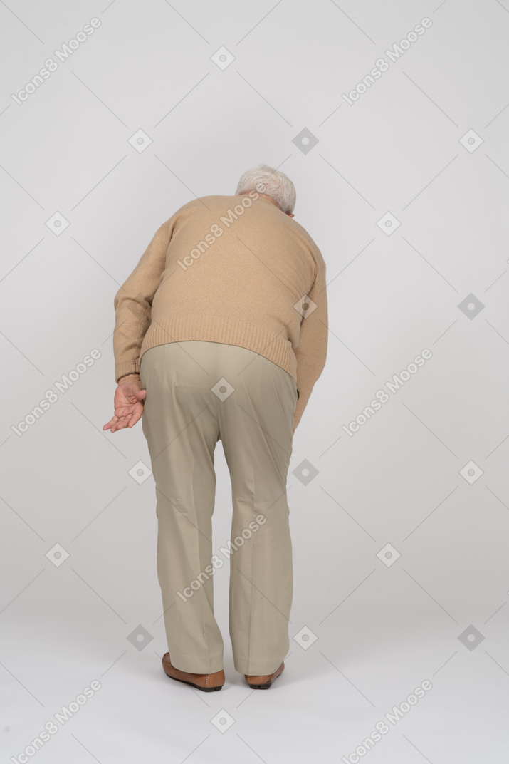 Retrovisione di un vecchio in abiti casual che si china e si tocca il ginocchio dolorante