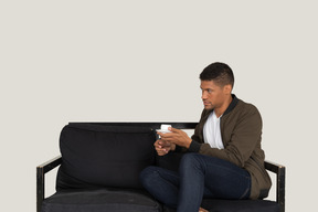 Three-quarter view of a young dreaming man sitting on a sofa with a cup of coffee