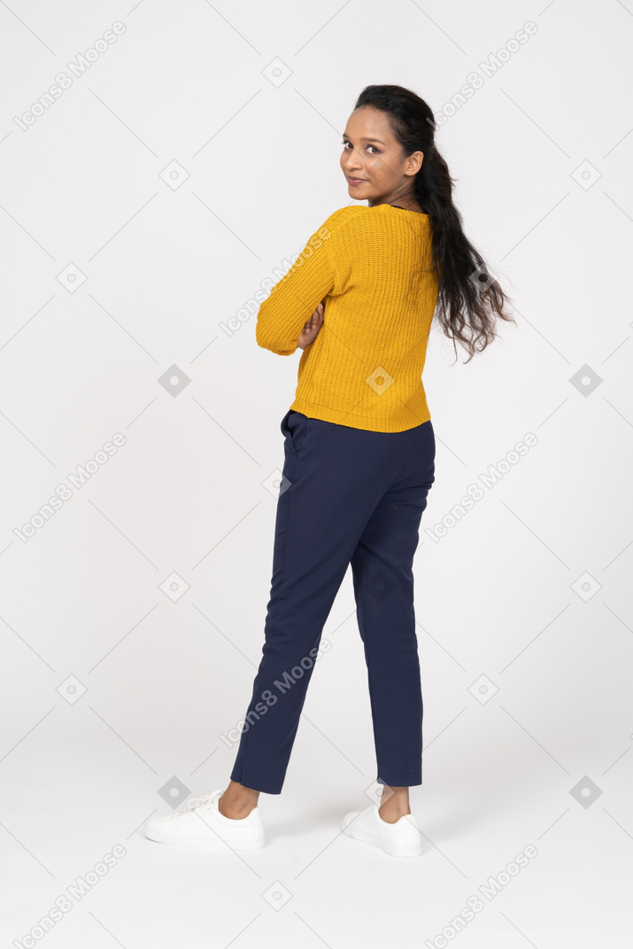 Rear view of a girl in casual clothes posing with crossed arms and looking at camera