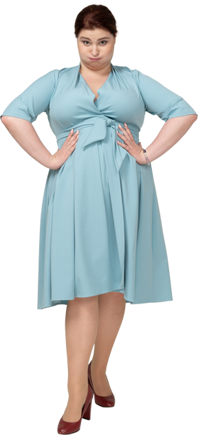 Vista frontal de uma mulher de vestido azul em pé com as mãos na cintura e fazendo caretas