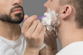 Close-up of young man shaving another man's face