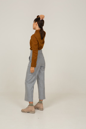 Three-quarter back view of a young asian female in breeches and blouse touching head