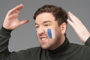 Fan de football masculin de trois quarts avec art visage bleu et blanc levant les mains