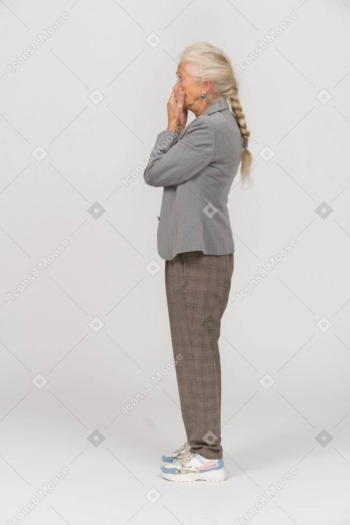 Vista lateral de una anciana asustada en traje cubriendo la boca con las manos