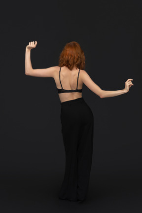 A back side view of the cute young woman dressed in black dancing on the black background