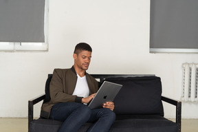 一个无聊的年轻人坐在沙发上看平板电脑的前视图