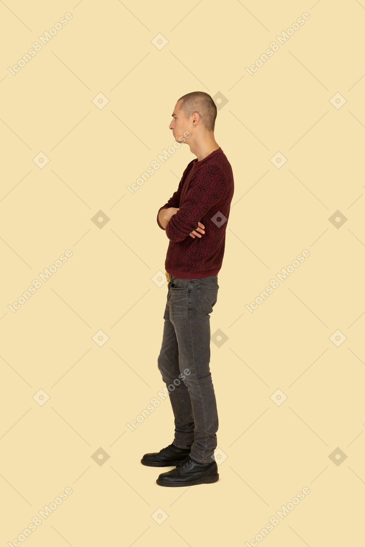 Side view of an offended young man dressed in casual clothes crossing his hands