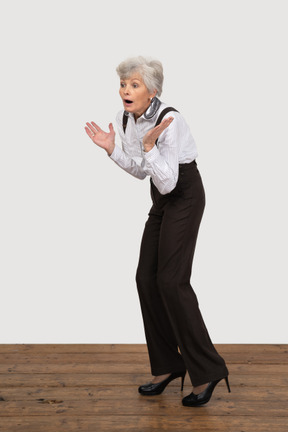 Three-quarter view of a surprised old lady in office clothing raising hands