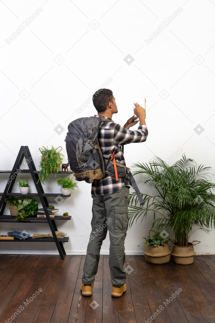 Vista traseira de três quartos de um turista com uma mochila escrevendo em seu planejador