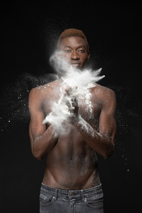 Close-up a young male clapping with flour in his palms looking at camera