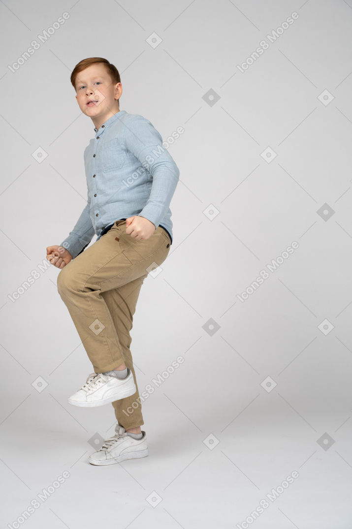 Side view of a cute boy standing on one leg