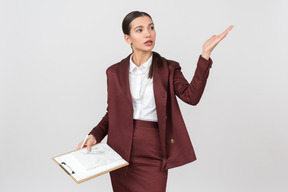 Atractiva mujer vestida formalmente con un portapapeles apuntando a algo.