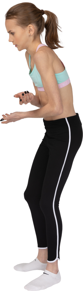 Vista lateral de una jovencita en ropa deportiva doblando mientras levanta las manos