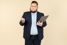 Young overweight office worker seems like not getting something and holding digital tablet