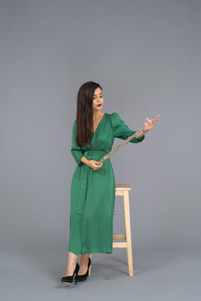 Vorderansicht einer jungen dame im grünen kleid, die auf einem stuhl sitzt und klarinette hält
