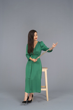 Front view of a young lady in green dress sitting on a chair and holding clarinet