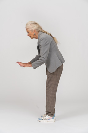 Vista lateral de una anciana agachándose y mostrando la señal de alto