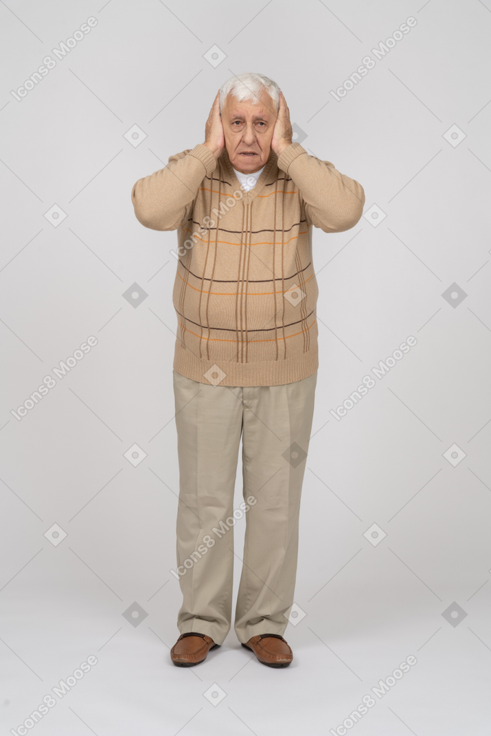 一个穿着休闲服的害怕老人用手捂住耳朵，看着相机的正面图