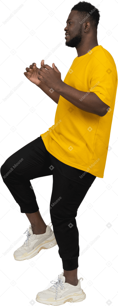 Vista lateral de um jovem de pele escura em uma camiseta amarela levantando a perna
