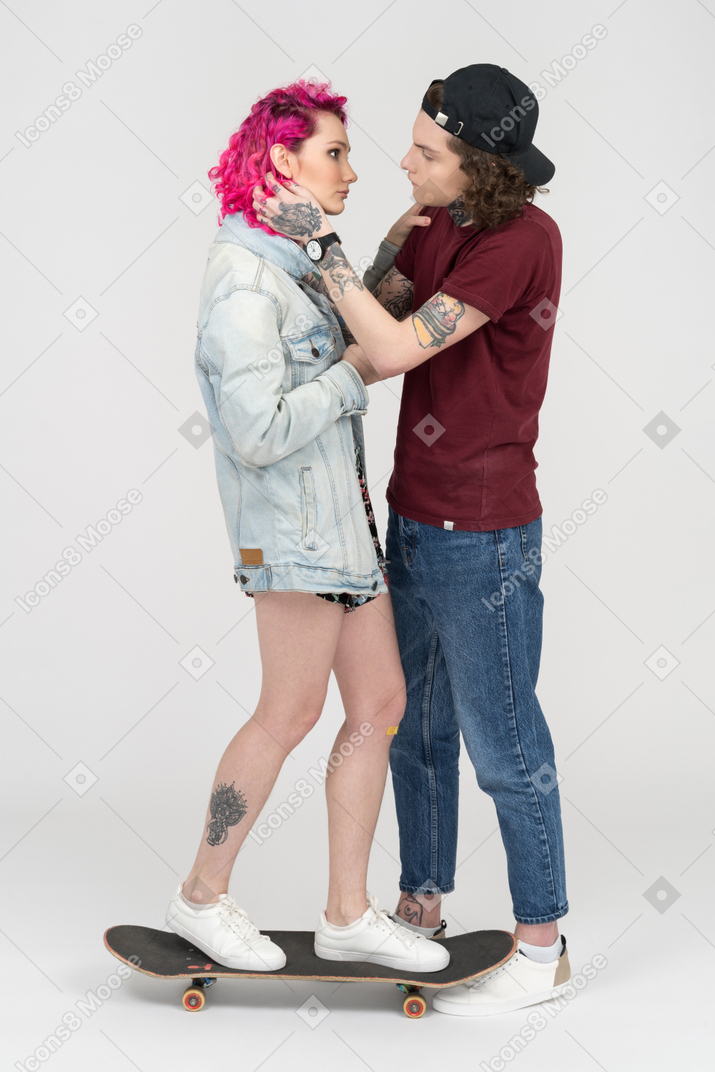 문신을 한 젊은 남자가 그의 분홍색 머리 여자 친구에게 키스하려고합니다.