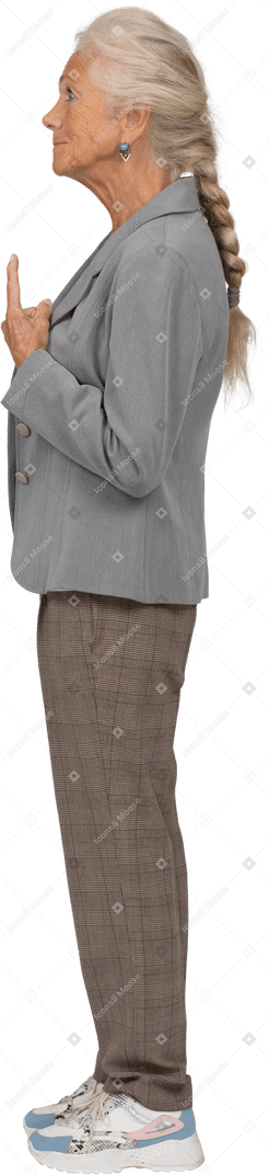 Vista laterale di una vecchia donna in abito che punta in alto con un dito