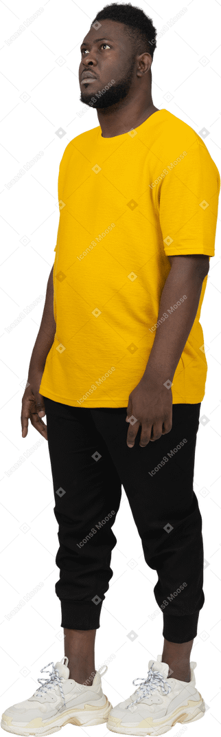 Vista de tres cuartos de un joven de piel oscura con camiseta amarilla parado
