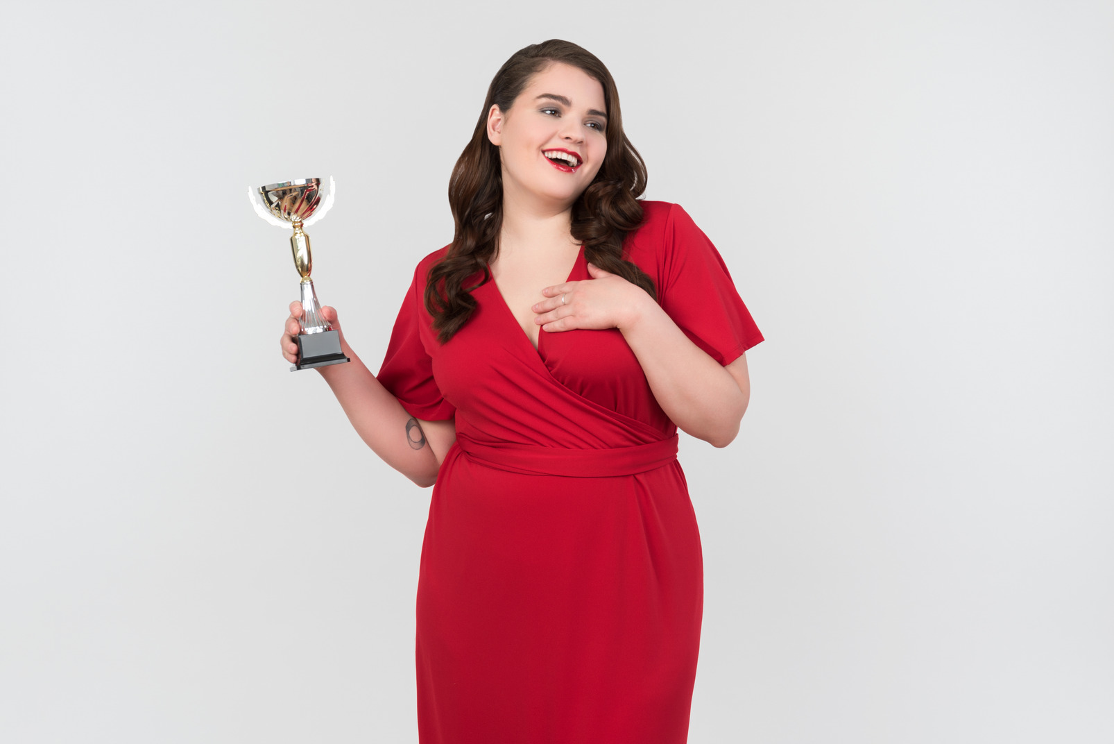 Smiling young plus-size model in red evening dress holding trophy
