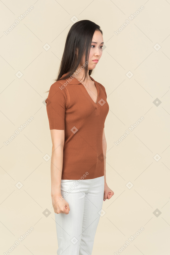 Offended young asian woman with clenched fists standing half sideways
