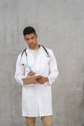 A man in a white lab coat writing on a clipboard