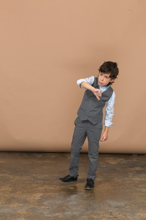 Vista frontal de um menino bonito de terno cinza, mostrando o polegar para baixo
