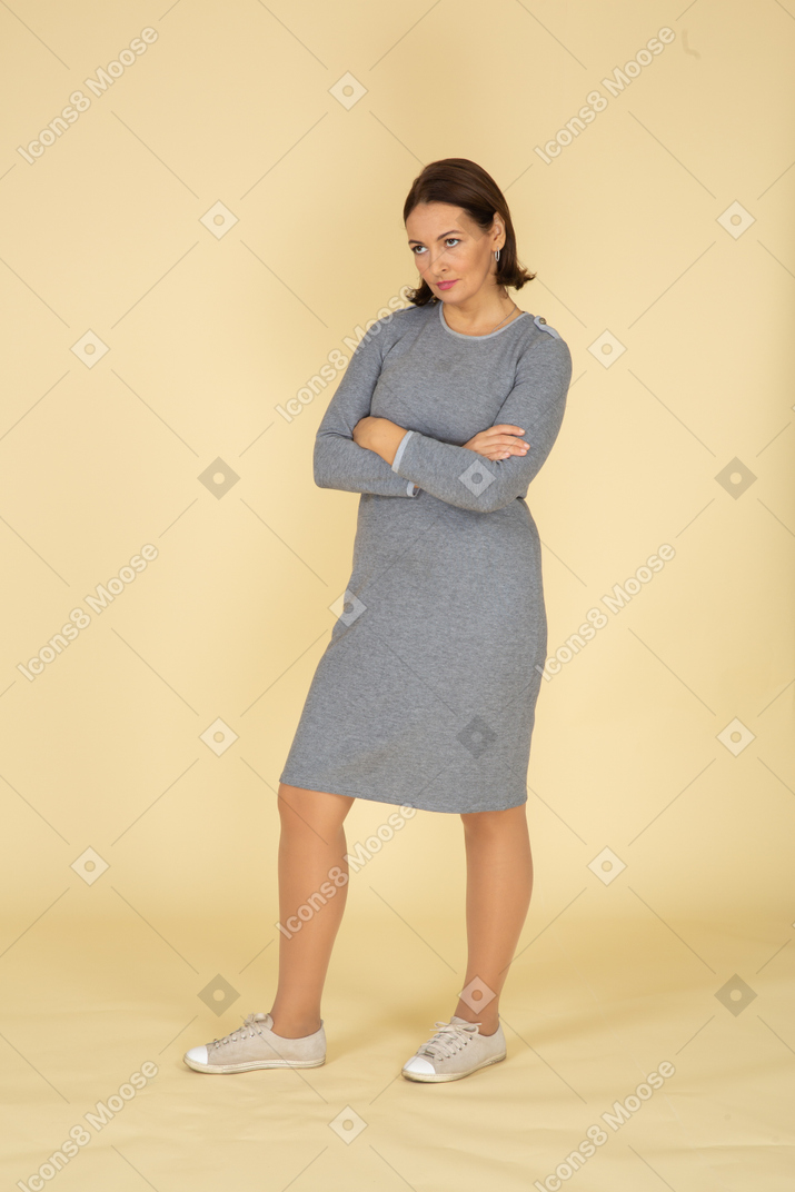 Vista frontal de uma mulher de vestido cinza posando com os braços cruzados