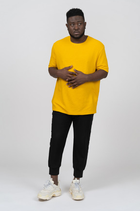 Vista frontal de un joven de piel oscura con camiseta amarilla tomados de la mano en el estómago