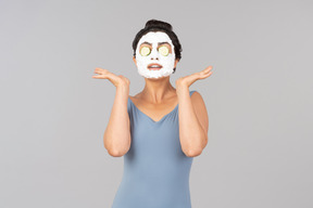 Woman with white facial mask and cucumber slices