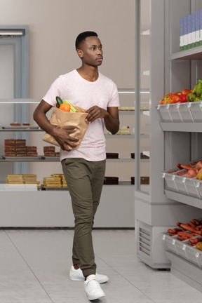 Uomo che cammina intorno a un supermercato con un sacchetto di generi alimentari