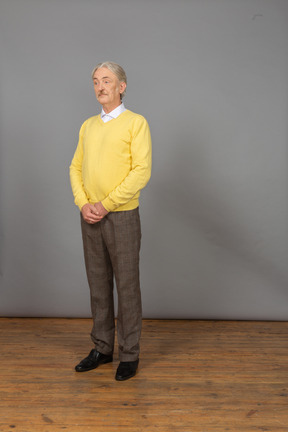 Three-quarter view of a confused old man holding hands together and wearing yellow pullover