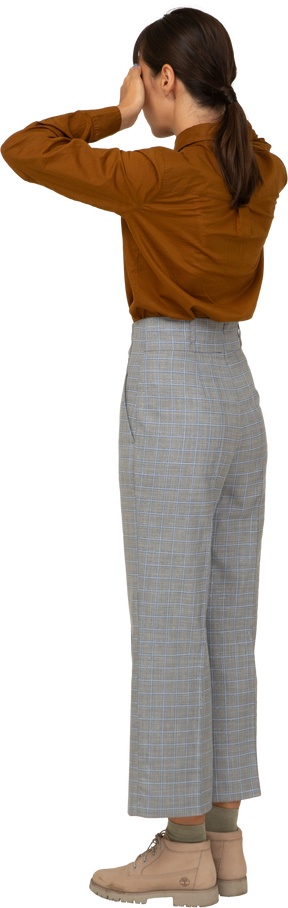 Vista posteriore di tre quarti di una giovane donna asiatica in calzoni e camicetta che nasconde gli occhi