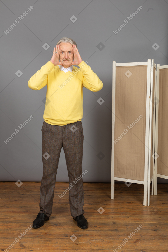 一个老人看着相机时举起他的手的前视图