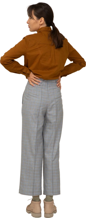 Back view of a young asian female in breeches and blouse putting hands on hips