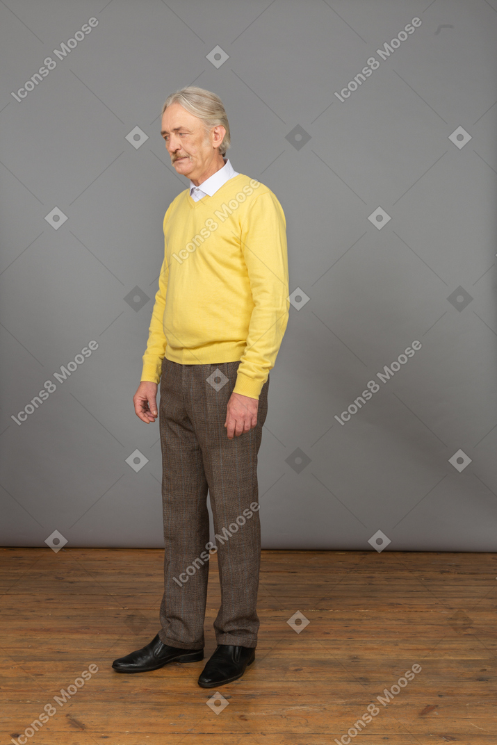 一个不高兴的老人，穿着黄色套头衫，放在一边看的四分之三视图