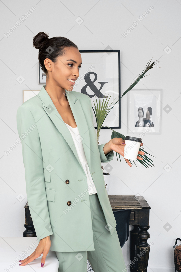 Donna di colore in piedi in ufficio e in possesso di tazza di caffè