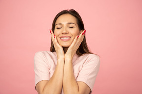 Ragazza attraente che sorride e che tocca la sua faccia con entrambe le mani