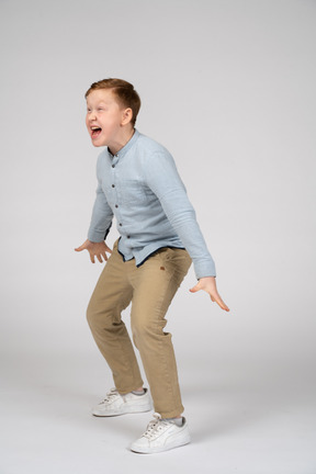 Vista lateral de um menino bravo em pé com os braços estendidos