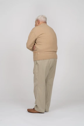 Side view of an old man in casual clothes standing with crossed arms