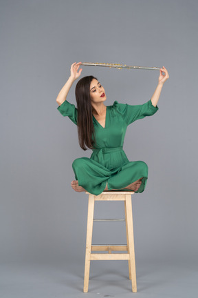 A figura intera di una giovane donna che tiene il suo clarinetto sopra la testa mentre è seduto su una sedia di legno