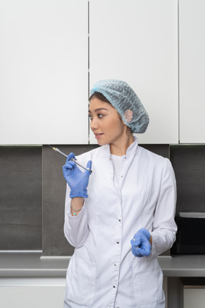 Vista frontal de una doctora con un sombrero médico sosteniendo una jeringa y mirando a un lado