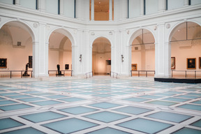 A big empty hall of an art exhibition, with paintings and statues in the background