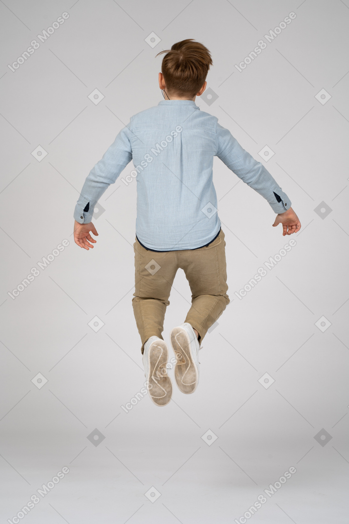 Back view of a boy in blue shirt and white sneakers jumping