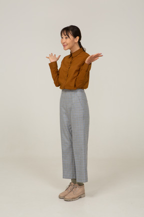 Three-quarter view of a delighted young asian female in breeches and blouse raising hands